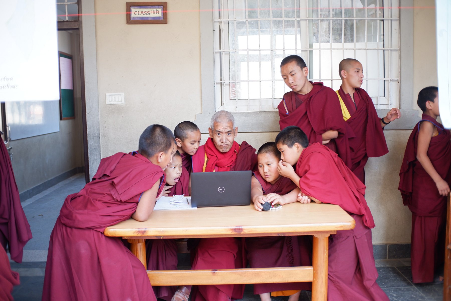 a group of monks sitting around a table with a laptop